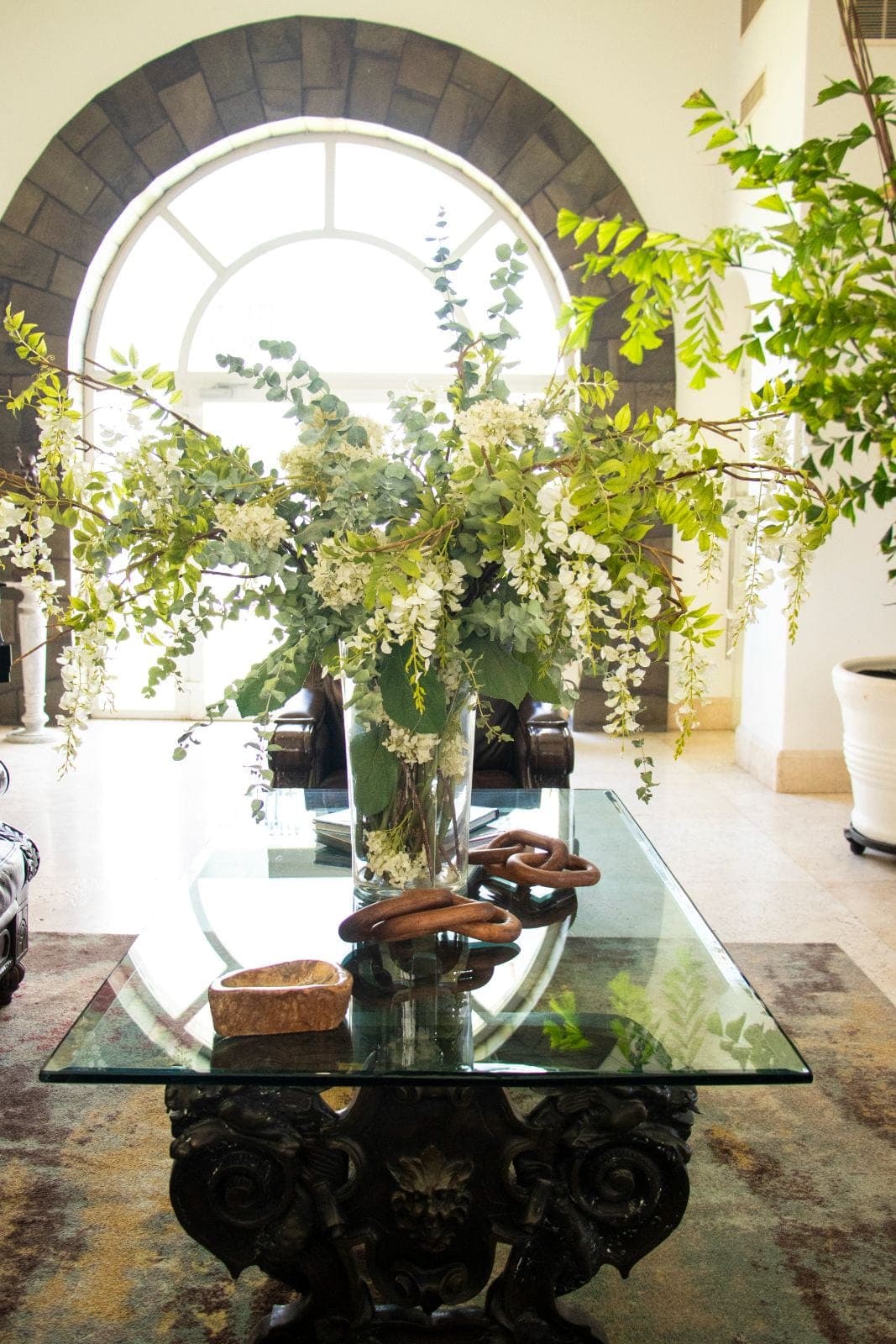 Vestíbulo con arco de piedra y arreglo floral sobre mesa antigua