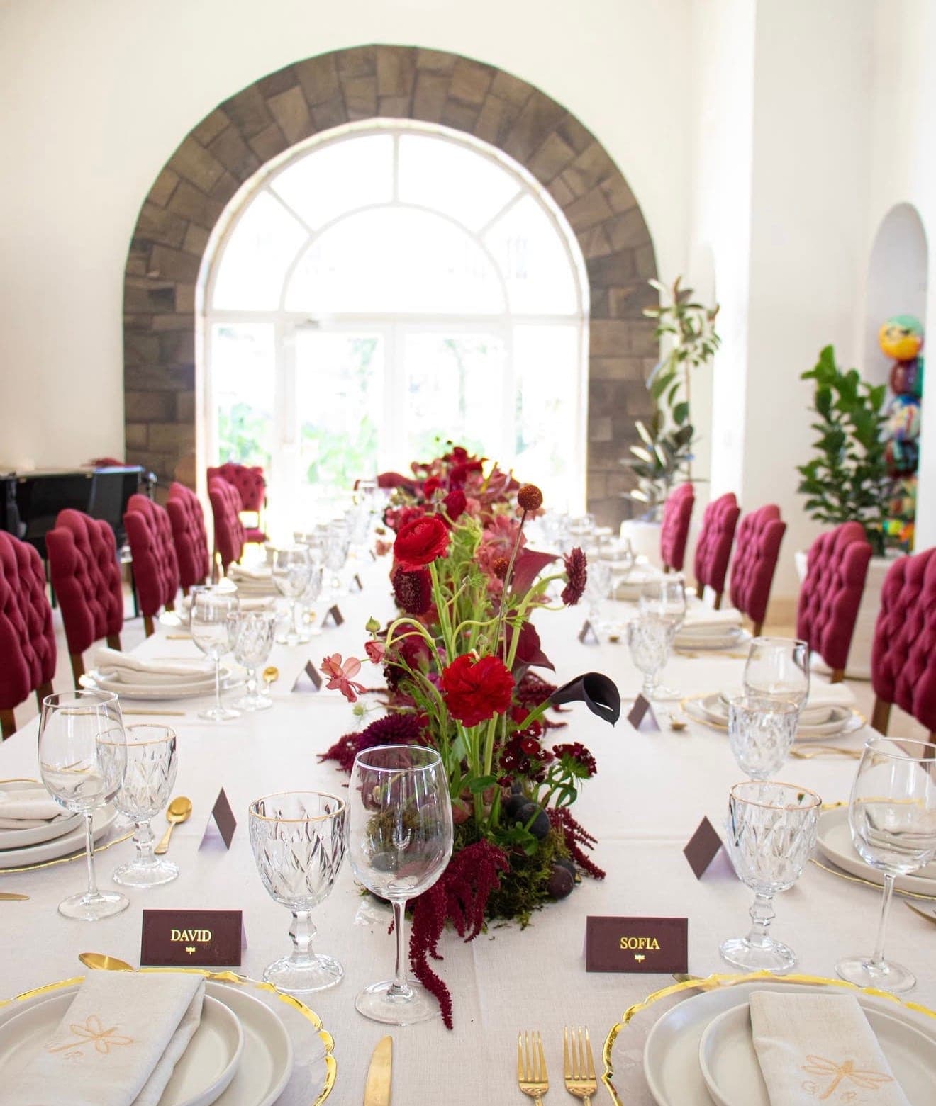Salón con arco de piedra, mesa imperial y flores en tonos vino